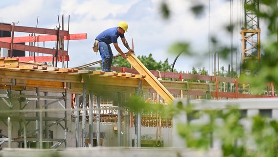 Ein Bauarbeiter nimmt auf einer Baustelle einen Balken entgegen. (Symbolfoto) © picture alliance / Sven Simon Foto: Frank Hoermann/SVEN SIMON