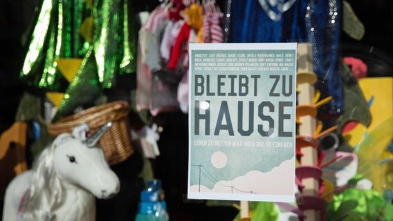 Ein Plakat mit der Aufschrift "Bleibt zu Hause" hängt im Schaufenster eines geschlossenen Spielzeuggeschäfts in Hamburg. © picture alliance/dpa Foto: Christian Charisius