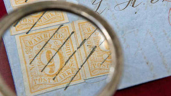 Ein Brief mit der größten bekannten Anzahl von 9-Schilling-Briefmarken aus dem Jahr 1859, der aus der Sammlung Erivan stammt, liegt im Heinrich Köhler Auktionshaus unter einer Lupe. © picture alliance / dpa Foto: Sebastian Gollnow