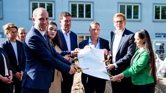 Vertreter der Hamburgischen Bürgerschaft zerschneiden auf dem Gelände der ehemaligen Bornplatz-Synagoge eine Kopie eines Dokuments mit dem Auftrag der Nationalsozialisten zur Zerstörung der Synagoge. © picture alliance/dpa Foto: Daniel Bockwoldt