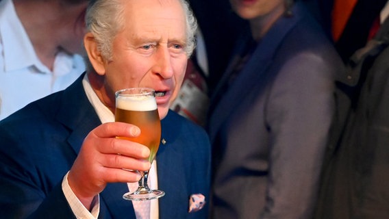 Charles hält ein selbst gezapftes Bier bei dem von der britischen Botschaft ausgerichteten feierlichen Empfang im Schuppen 52. © dpa-Bildfunk Foto: Jonas Walzberg/dpa