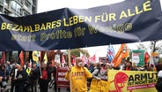 Demonstrationsteilnehmer halten ein Transparent mit der Aufschrift "Bezahlbares Leben für alle statt Profite für Wenige". © Markus Scholz/dpa 
