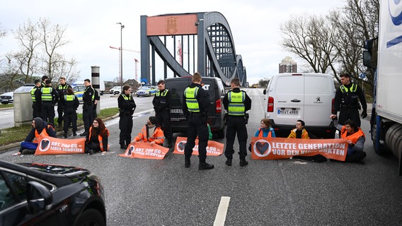 Klimaaktivisten der Bewegung "Letzte Generation" blockieren in Hamburg die Elbbrücken stadteinwärts. Vor ihnen stehen Polizisten, hinter ihnen zwei Transporter. © picture alliance / dpa Foto: Jonas Walzberg