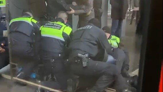 Sechs Mitarbeitende der Polizei und der Hochbahnwache fixieren einen Menschen am Boden. © NDR Foto: Schirin R.