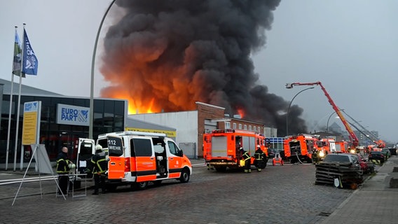 Feuerwehrleute und Löschfahrzeuge stehen in Rothenburgsort bei einem Großbrand auf einem Autohof. © NEWS5 