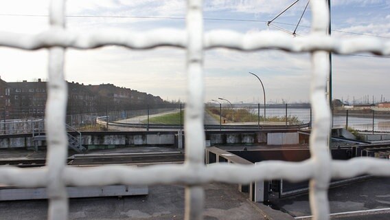 Durch weiße Gitterstäbe im Zaun ist der Freihafen von der Veddel aus zu sehen. © NDR Foto: Daniel Sprenger