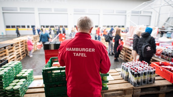 Ein Mann, der eine Jacke mit dem Schriftzug "Hamburger Tafel", steht an einer Ausgabestelle der Hamburger Tafel. © picture alliance/dpa Foto: Daniel Reinhardt