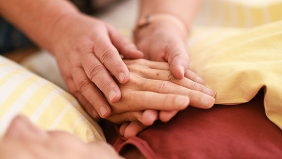 Eine Hospizmitarbeiterin hält die Hand eines todkranken Menschen, der im Hospiz im Bett liegt © picture alliance/dpa | Felix Kästle Foto: Felix Kästle