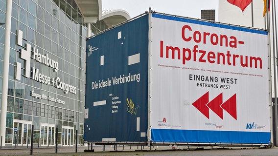 Ein Transparent mit der Aufschrift "Corona-Impfzentrum Eingang West" steht vor dem Haupteingang der Hamburger Messehallen. © picture alliance / dpa Foto: Georg Wendt
