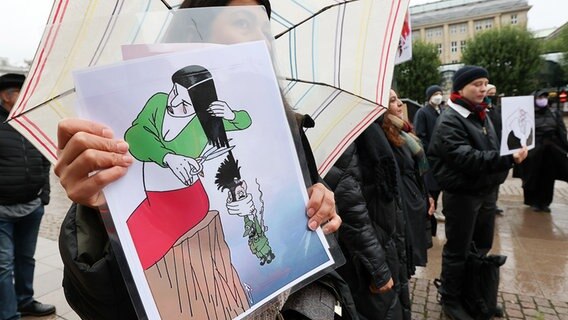 Während einer Demonstration gegen das politische Regime im Iran hält eine Frau ein Plakat mit einer Karikatur. © picture alliance/dpa Foto: Bodo Marks