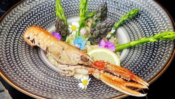 Eine Kaisergranat-Garnele ist mit grünem Spargel angerichtet.  Foto: Dave Hänsel