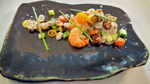 Weihnachtlicher Bratkartoffel-Salat mit Garnelen auf einem Teller serviert. © NDR Foto: Dave Hänsel