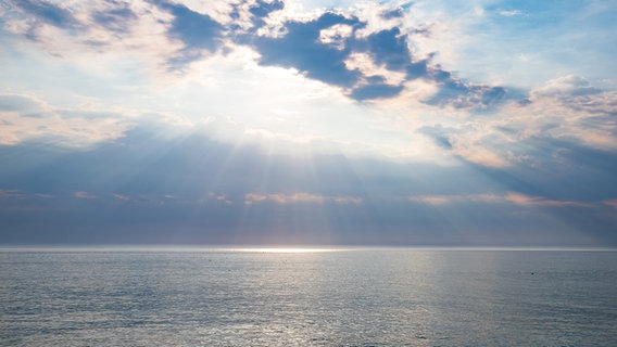 Sonnenstrahlen durchbrechen die Wolken über der ruhigen Nordsee vor Sylt. © picture alliance Foto: Jens Hogenkamp