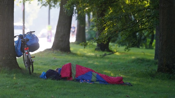 Ein Obdachloser liegt auf einer Wiese an der Kennedybrücke in seinem Schlafsack neben seinem Fahrrad. © picture alliance/dpa | Marcus Brandt Foto: Marcus Brandt