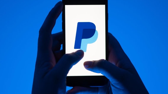 Eine Frau hält ein Smartphone in den Händen, auf dem das Logo des Bezahldienstes Paypal zu sehen ist. © Sebastian Kahnert/dpa 