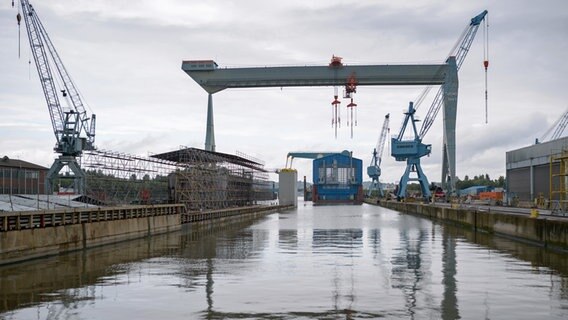 Kräne und ein Trockendock spiegeln sich im Wasser der leeren Werftanlage der Pella Sietas Werft in Hamburg. © picture alliance / dpa Foto: Jonas Walzberg