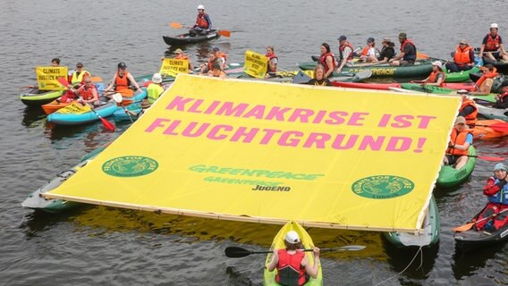 Mitglieder von Greenpeace und Fridays for Future mit Kajaks, Schlauchbooten und einem großen Banner mit der Aufschrift "Klimakrise ist Flüchtlingsgrund!" auf der Binnenalster in Hamburg. © picture alliance / dpa Foto: Bodo Marks