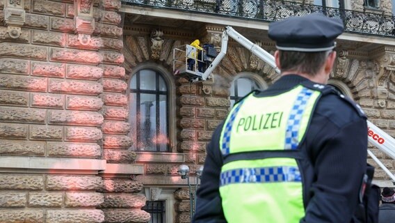 Ein Polizist steht vor dem Eingang des Hamburger Rathauses, das nach einer Farbattacke gereinigt wird. © dpa Foto: Bodo Marks