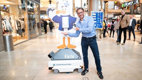 Der Schauspieler Patrick Bach stellt einen Service-Roboter namens "Fiete" vor. Das Gerät soll auf Wunsch Hand-Desinfektionsmittel an Besucher eines Einkaufscenters verteilen. © picture alliance / dpa Foto: Daniel Reinhardt