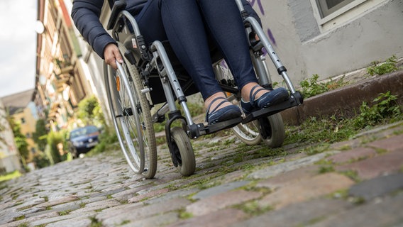 Eine Frau im Rollstuhl fährt in Hamburg über Kopfsteinpflaster. © picture alliance/dpa-tmn Foto: Christin Klose