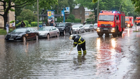 Eine Feuerwehrfrau steht im Stadtteil Öjendorf auf einer von starkem Regen überfluteten Straße. © picture alliance/dpa | Daniel Bockwoldt Foto: Daniel Bockwoldt