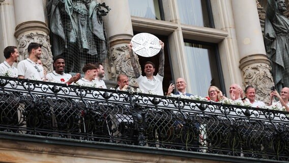 FC St. Pauli-Trainer Fabian Hürzeler hält eine gebastelte Meisterschale zwischen seiner Mannschaft und dem Team auf dem Balkon des Rathauses. © picture alliance/dpa Foto: Christian Charisius