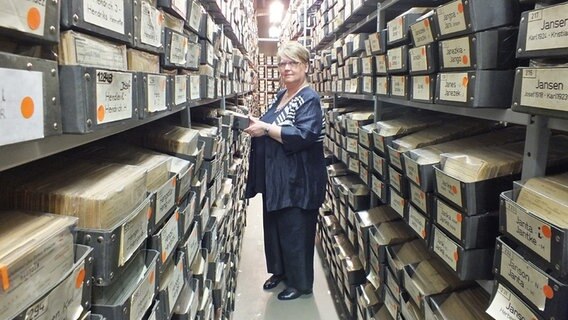 Kirsten Bollin, Leiterin der DRK-Suchdienstes in Hamburg, steht vor Archiv-Regalen der Zentralen Namenskartei in Hamburg.  Foto: Marc-Oliver Rehrmann