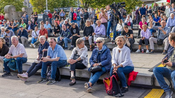 Besucherinnen und Besucher sitzen vor der NDR Bühne zu den Feierlichkeiten am Tag der Deutschen Einheit. © NDR Foto: Axel Herzig