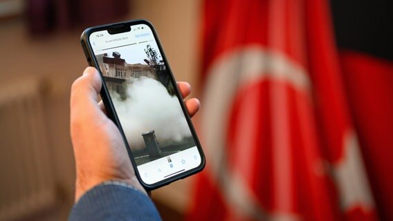 Ein Mann in Hamburg zeigt auf dem Handy das Video eines einstürzenden Hauses von seinen Familienmitgliedern aus dem Erdbebengebiet in der Türkei. © picture alliance / dpa 