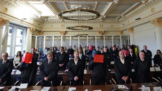 Die Angeklagten stehen neben ihren Anwälten im Prozess um Vergewaltigung einer Jugendlichen im Stadtpark im Sitzungssaal im Strafjustizgebäude und halten sich Aktenordner vor das Gesicht. © picture alliance/dpa/Pool-dpa Foto: Marcus Brandt