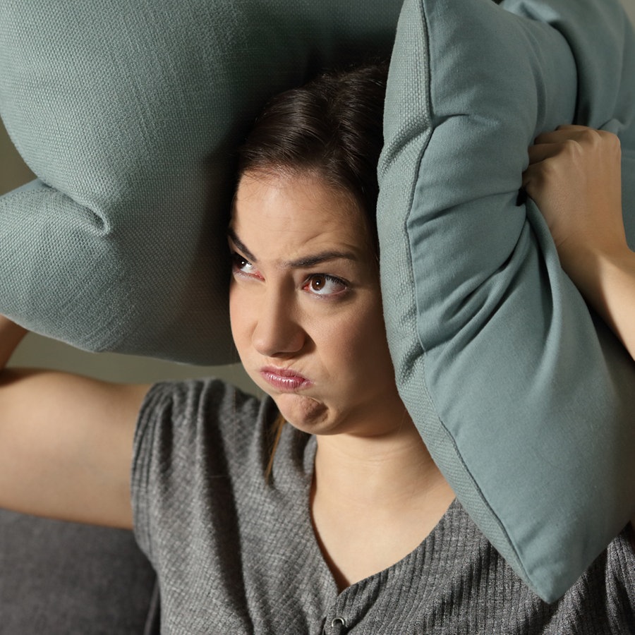 Eine Frau drückt sich gestresst zwei Kissen auf die Ohren. © Colourbox Foto: #81285