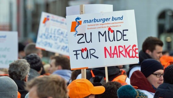 Ärzte von Unikliniken halten bei einem Warnstreik in Hannover unter anderem ein Schild mit der Aufschrift "Zu müde für Narkose" hoch. (Archivbild vom 4.2.2020) © picture alliance/dpa | Julian Stratenschulte 