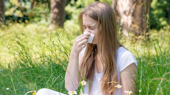 Eine junge Frau sitz im Gras und schnäuzt sich die Nase in ein Taschentuch. © colourbox Foto: -