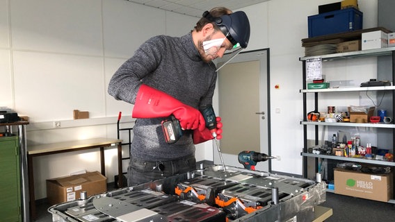 Geschäftsführer Lasse Bartels von LB Systems öffnet mit einem Werkzeug eine E-Auto-Batterie. © NDR Foto: Simon Hoyme