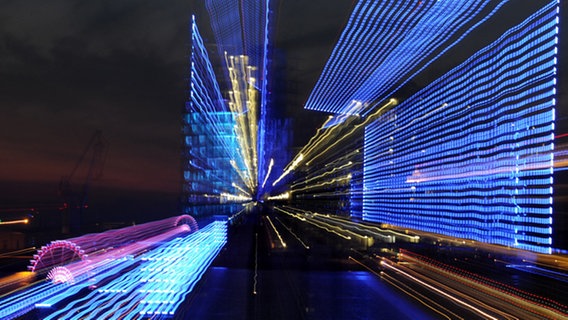 Die Baustelle der Elbphilharmonie, der Michel und Hafenkräne in blaues Licht getaucht (Aufnahme durch Zoomeffekt). © dpa Foto: Angelika Warmuth