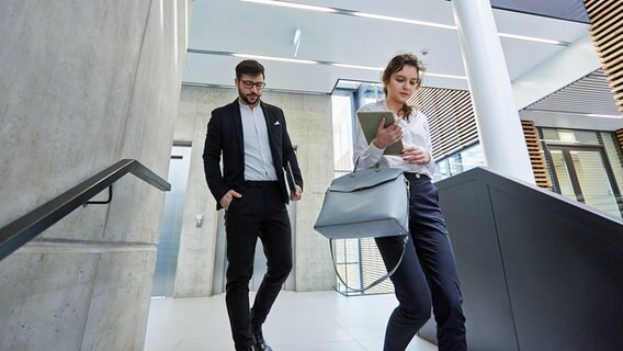 Ein Mann und eine Frau sind in einem Bürogebäude eilig im Treppenhaus unterwegs. © dpa picture alliance / Zoonar Foto: Robert Kneschke