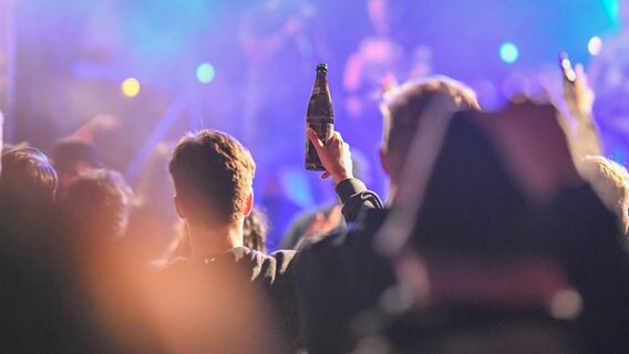 Menschen halten in einem Club ihre Hände und eine Bierflasche in die Luft. © picture alliance / Marius Bulling | Ostalb Network 