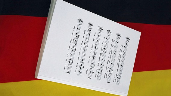 Eine Strophe in Noten vom "Lied der Deutschen" liegt auf einer deutschen Nationalfahne. © Imago/Steinbach 