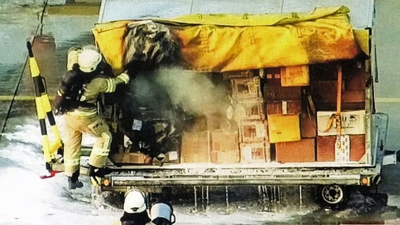 Feuerwehrleute löschen ein brennendes Paket in einem Frachtwagen am Flughafen Leipzig. © NDR, WDR, SZ 
