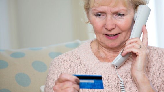 Seniorin telefoniert während sie ihren Blick auf eine EC-Karte in ihrer Hand richtet. © colourbox Foto: -