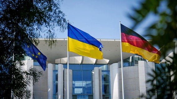 Die Fahne der Ukraine weht zwischen der europäischen (l.) und deutschen Fahne (r.) vor dem Bundeskanzleramt in Berlin. © Kay Nietfeld/dpa 