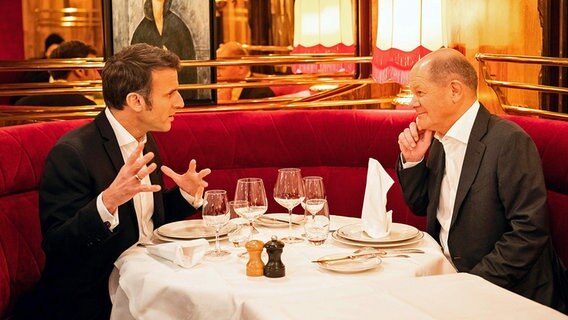Emmanuel Macron (l.), Präsident von Frankreich, und Bundeskanzler Olaf Scholz (SPD) sitzen bei einem Essen zusammen an einem Tisch in einem Restaurant. © dpa bildfunk/Bundesregierung Foto: Steffen Kugler