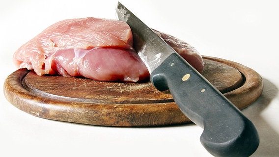 Rohes Geflügelfleisch und ein Messer liegen auf einem Schneidebrett. © imago stock & people 