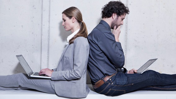 Eine Frau und ein Mann sitzen Rücken an Rücken und schauen auf ihre Laptops, die auf ihren Beinen liegen. © picture alliance / Westend61 | Westend61 / Jo Kirchherr 