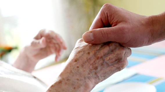 Ein Pfleger hält in einem Pflegeheim die Hand einer bettlägerigen Bewohnerin. © dpa Foto: Oliver Berg