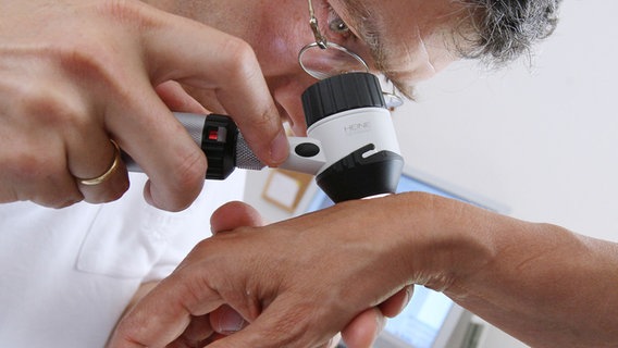 Ein Hautarzt untersucht mit einer Lupe die Haut eines Patienten. © picture alliance Foto: Karl-Josef Hildenbrand