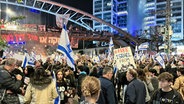 Angehörige und Unterstützer der israelischen Geiseln, die im Gazastreifen von der islamistische Hamas festgehalten werden, blockieren eine Straße während einer Kundgebung in Tel Aviv, bei der ihre Freilassung gefordert wird. Sie protestieren auch gegen die Regierung und fordern Neuwahlen. © Cindy Riechau/dpa 