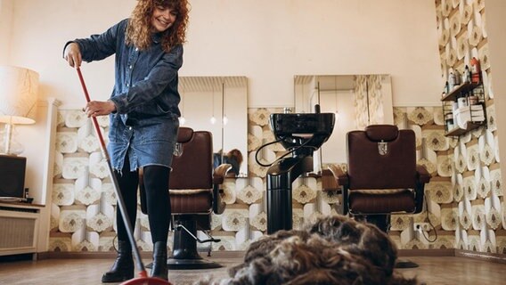 Janine Falke fegt in ihrem Friseursalon abgeschnittnes Haar zusammen. © Anne Juka Foto: Anne Juka