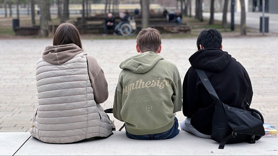 Drei Jugendliche sitzen in München in einem Park nebeneinander. © picture alliance / SvenSimon | FrankHoermann 