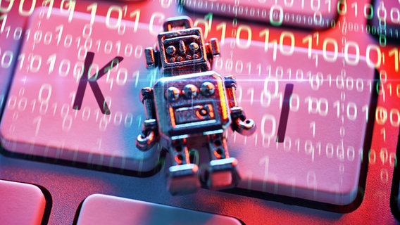 Eine Roboterfigur liegt auf einer Computertastatur mit der Aufschrift KI. Symbolfoto Künstliche Intelligenz © picture alliance / CHROMORANGE | Christian Ohde 
